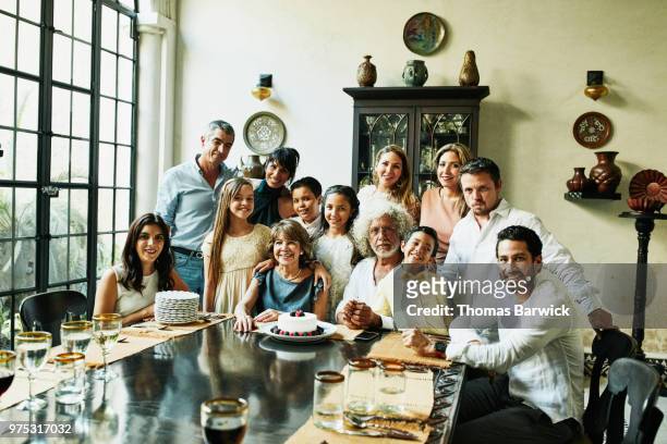 portrait of multigenerational family gathered in dining room during celebration dinner - woman holding cake stock-fotos und bilder
