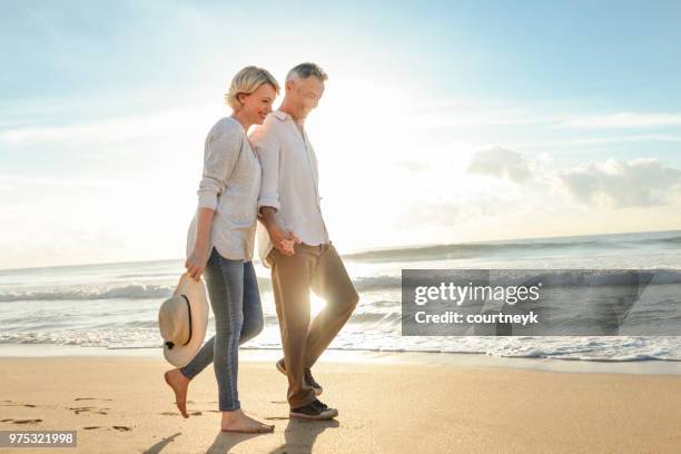 äldre par promenader på stranden vid solnedgången eller soluppgång. - mature couple bildbanksfoton och bilder