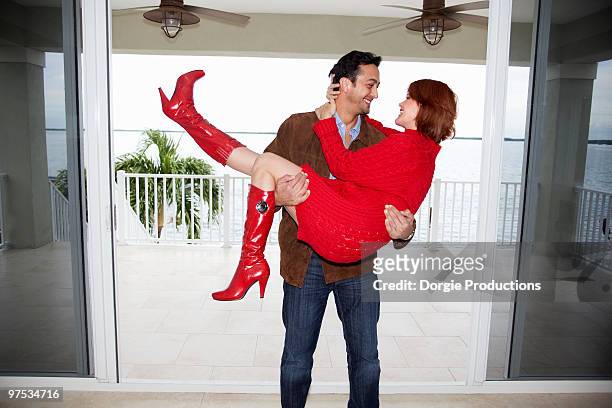 man carries a woman romantically in his arms - red dress stock pictures, royalty-free photos & images