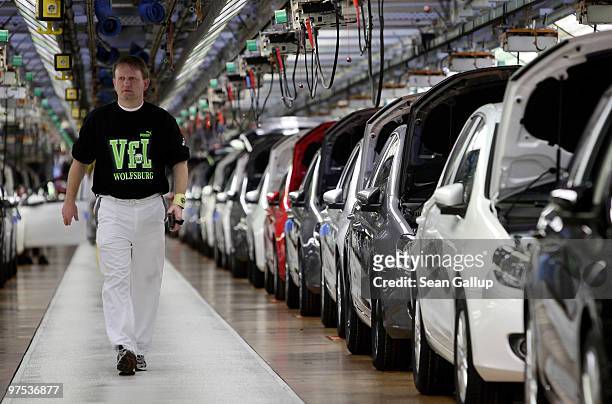 Worker wearing a VfL Wolfsburg shirt walks by finsihed Volkswagen Golf cars at the end of the assembly line at the VW factory on March 8, 2010 in...