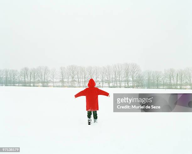 boy with red coat walking through snow field - snowfield stock pictures, royalty-free photos & images