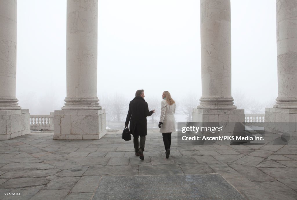 Businessman & woman walk thru white marble columns