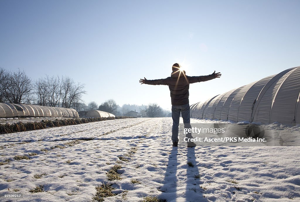 Man stands with outstretched arms near greenhouses