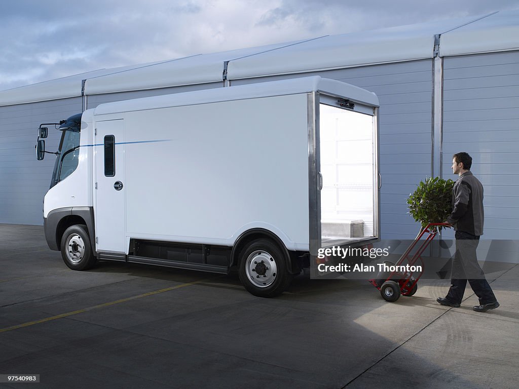 Man with trolley and plant walking to electric van