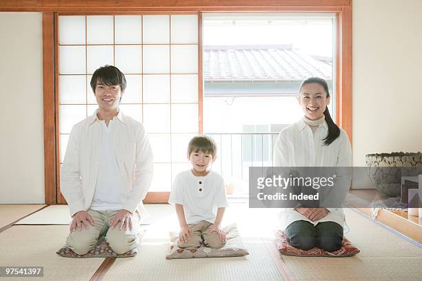two parents and son kneeling on cushions, smiling - fersensitz stock-fotos und bilder