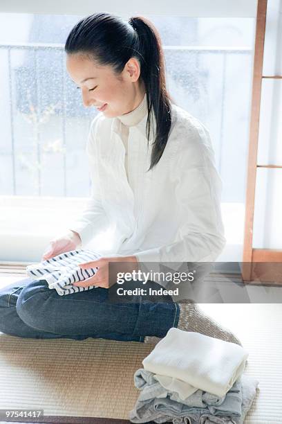 mid adult woman sitting and folding clothes - woman smiling facing down stock pictures, royalty-free photos & images