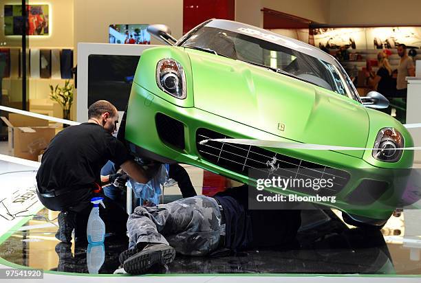 Employees install a Ferrari automobile in its position prior to the official opening of the Geneva International Motor Show in Geneva, Switzerland,...