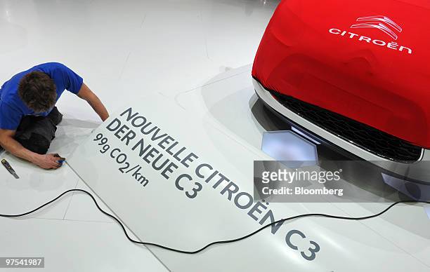 An employee installs a sign indicating the new Citroen C3 automobile at the company's stand prior to the official opening of the Geneva International...