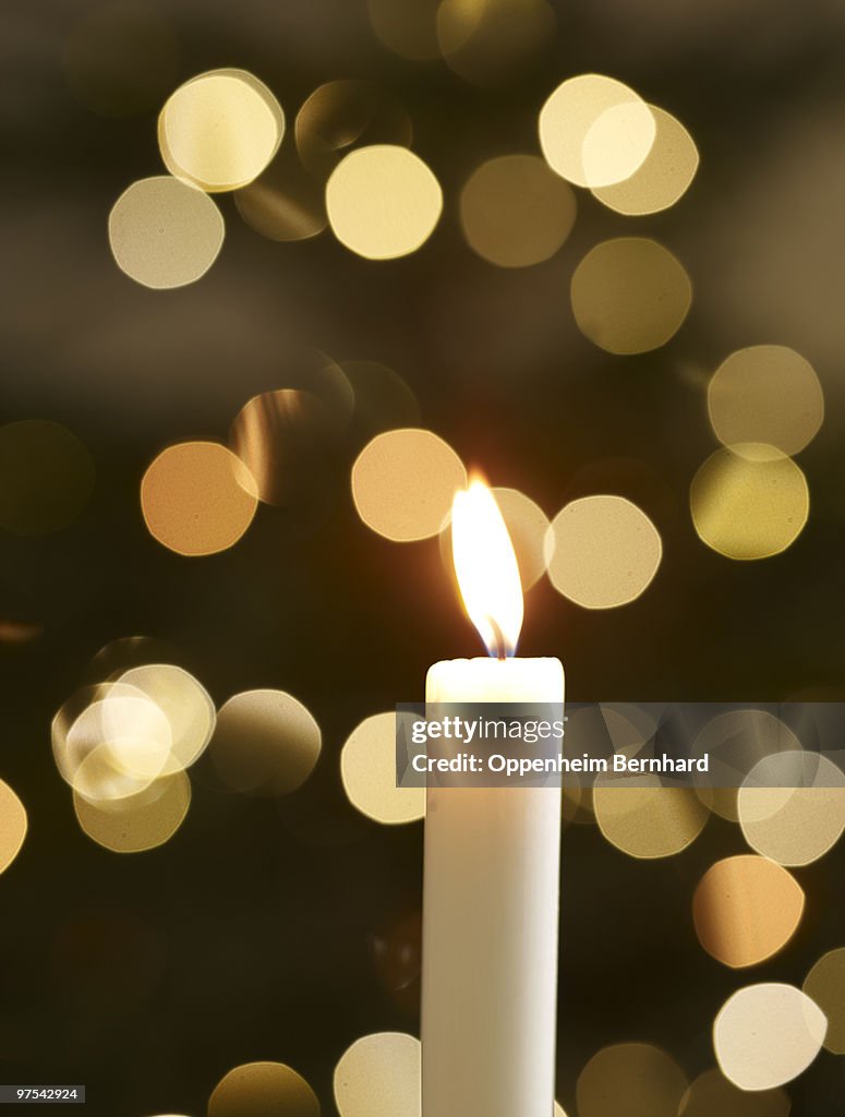 Single candle with christmas lights in background