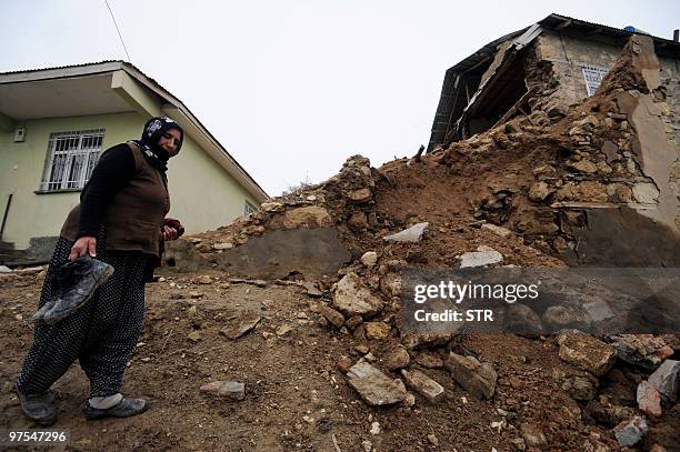 Woman walks among debris in front of a destroyed house in the village of Okcular, on March 8, 2010.A powerful pre-dawn earthquake buried sleeping...