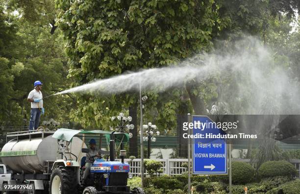 Employee of New Delhi Municipal Council Horticulture Department sprinkles water on trees in a bid to bring down dust near Vigyan Bhawan on June 15,...