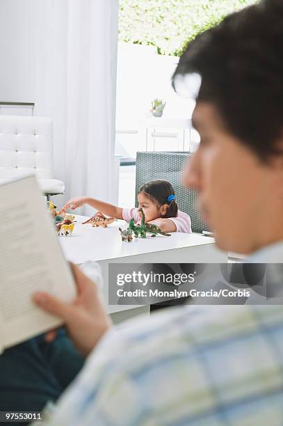 man reading and girl playing with toy dinosaurs - dinosaur toy i stock pictures, royalty-free photos & images