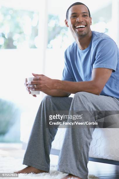 man sitting on bed holding cup - bettmann corbis stock-fotos und bilder