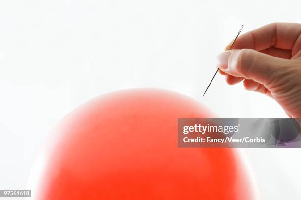 man's hand holding sewing needle over balloon - economic boom stock pictures, royalty-free photos & images