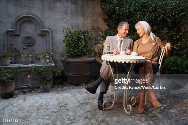 senior couple sitting at table in courtyard patio - eating secret stockfoto's en -beelden