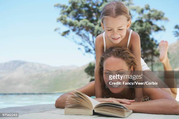 mother and daughter reading - woman lying on stomach with feet up foto e immagini stock