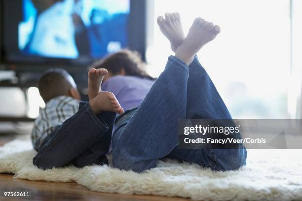 mother and son watching television - woman lying on stomach with feet up foto e immagini stock