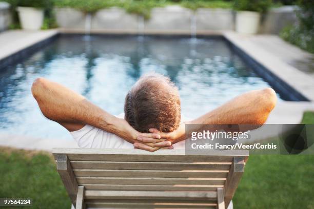 man sitting with hands behind head admiring swimming pool - back shot position stock pictures, royalty-free photos & images