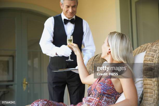 waiter serving glass of champagne to woman - valet stockfoto's en -beelden