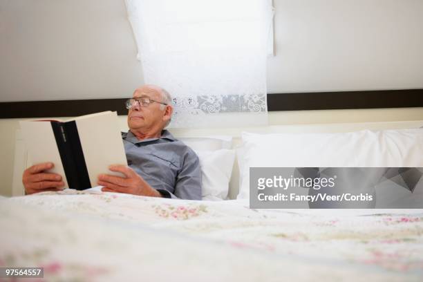senior man in bed - a woman modelling a trouser suit blends in with a matching background of floral print cushions stockfoto's en -beelden