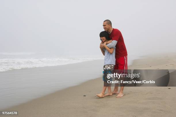 father hugging son on beach - capelli onde foto e immagini stock