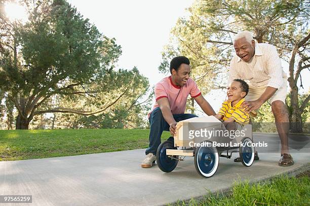 father and grandfather pushing boy in soapbox car - soapbox cart stock pictures, royalty-free photos & images