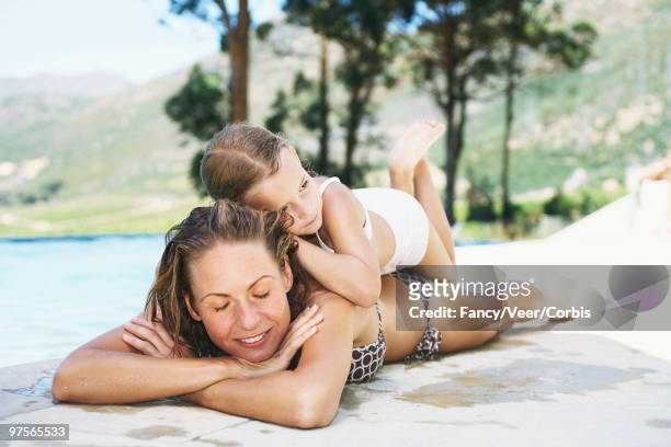 mother and daughter by a pool - woman lying on stomach with feet up foto e immagini stock