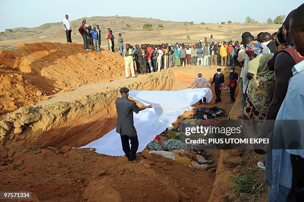 Natives of Dogo Nahawa village watch as health officials cover bodies of their kinsmen in a mass grave killed during a religious clash with the Hausa...