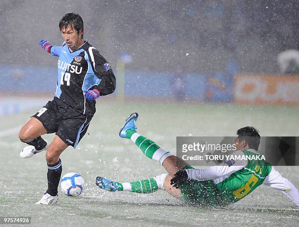 China's Beijing Guoan defender Xu Liang slides to clear the ball from Japanese club Kawasaki Frontale midfielder Yusuke Mori under heavy snow during...