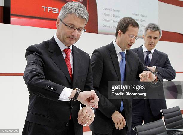 Rupert Stadler, chief executive officer of Audi AG, left, and Axel Strotbek, chief financial officer of Audi AG, center, check their watches with a...