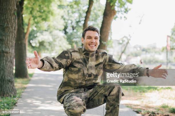 happy young soldier squatting in the park with hands outstretched - handsome military men stock pictures, royalty-free photos & images