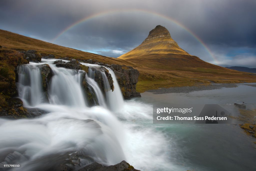 Kirkjufell waterfall under overcast sky with rainbow, Iceland