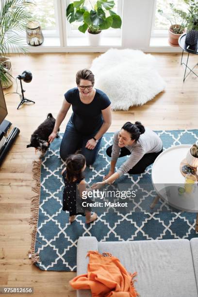 Mothers playing with daughter while sitting by dog in living room at home