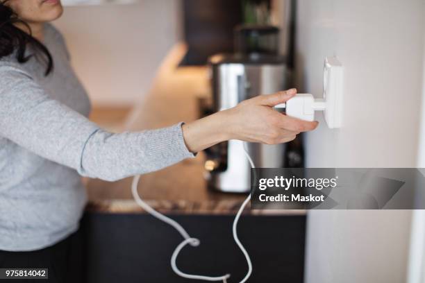 midsection of woman plugging mobile phone charger on wall at home - electric stockfoto's en -beelden