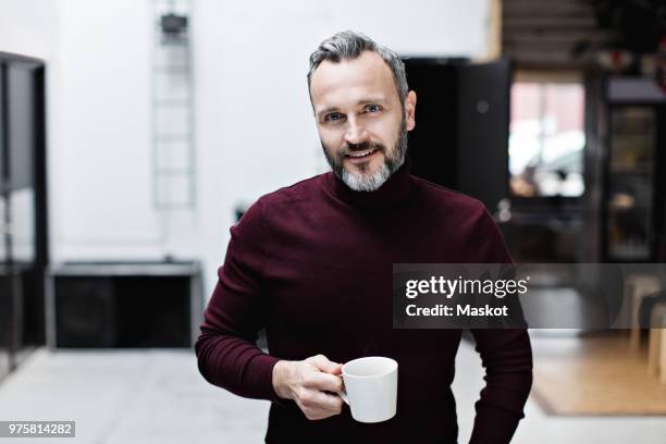 portrait of smiling mature businessman having coffee while standing at creative office - scandinavie photos et images de collection