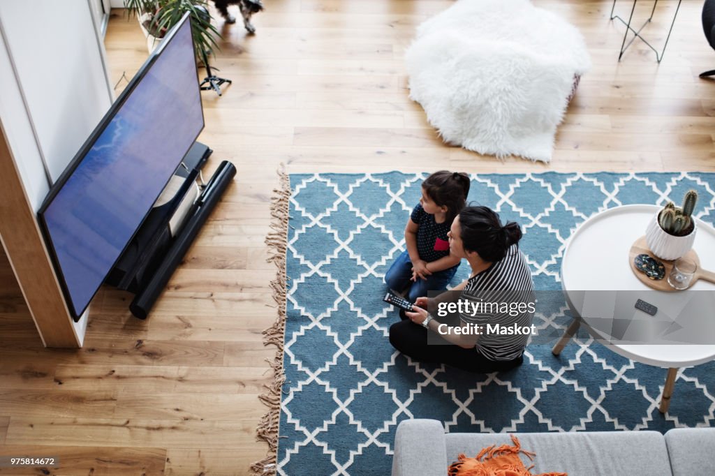 High angle view of mother and daughter watching television while sitting on floor at home