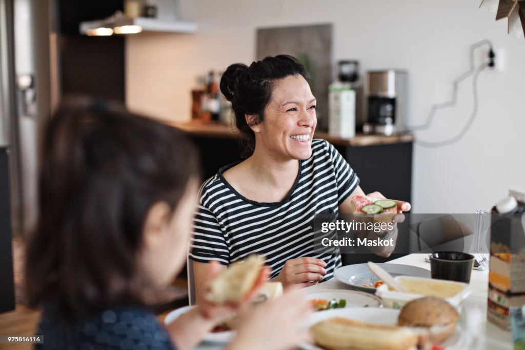 Smiling mother sitting with daughter while having breakfast at dining table