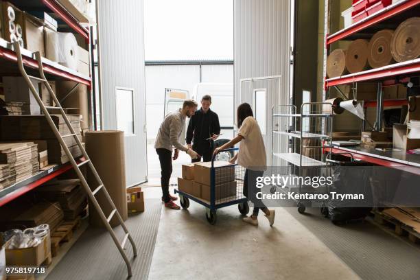female and male colleagues looking at boxes against delivery van - rollwagen stock-fotos und bilder