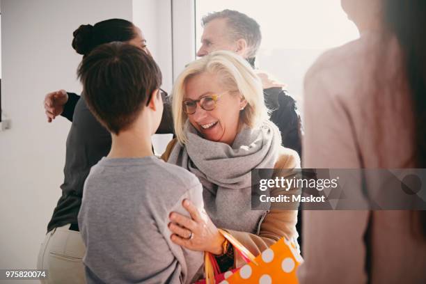 happy grandmother talking to grandson while senior father embracing daughter at home - wiedersehenstreffen stock-fotos und bilder