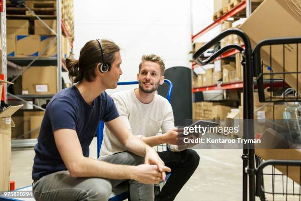 male colleagues discussing over digital tablet while sitting on push cart at industry - part time worker stock pictures, royalty-free photos & images