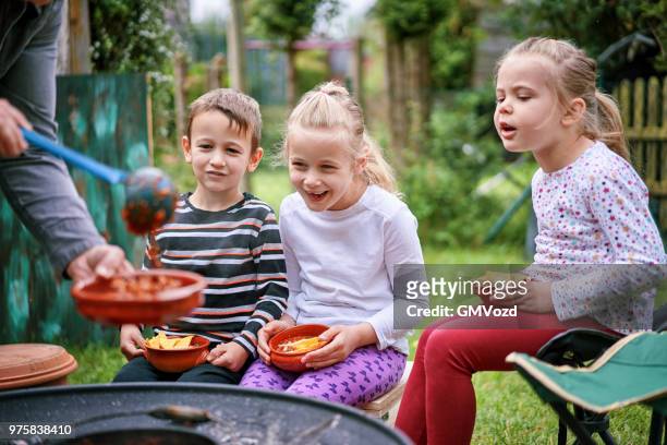 年輕的家庭吃辣椒騙子起重機在外面開放 logfire 前 - carne 個照片及圖片檔