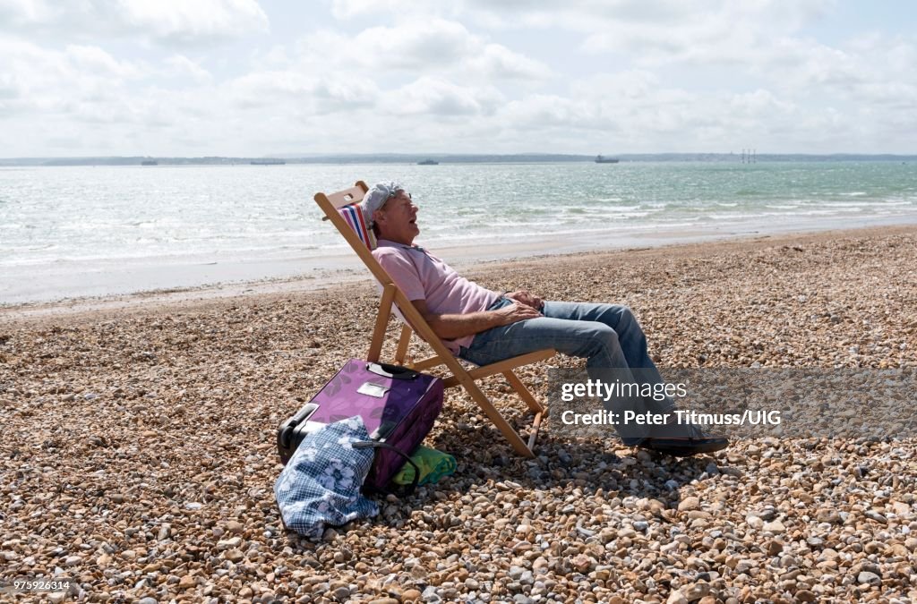 Elderly man wearing a knotted handkerchief on his head relaxing on the beach