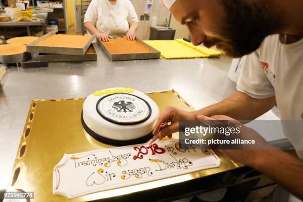 May 2018, Italy, Eppan: Pastry chef Rudolf Pertoll decorates a cake with the DFB logo and well wishes at the confectionery Peter Paul. The German...