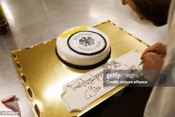 May 2018, Italy, Eppan: Pastry chef Rudolf Pertoll decorates a cake with the DFB logo and well wishes at the confectionery Peter Paul. The German...
