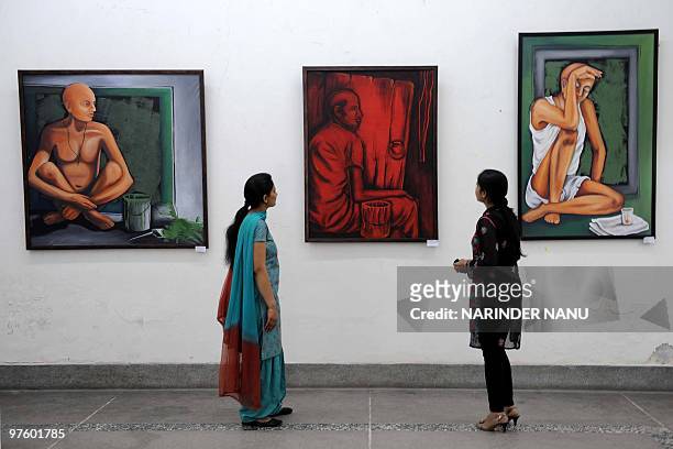 Indian visitors look at paintings on display during the opening of the annual art exhibition of paintings �Eventual Awakening� at the Indian Academy...