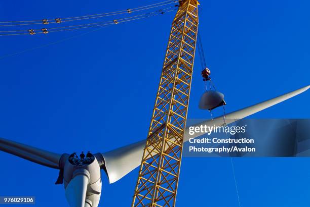 Two workers wait on the hub of a giant Enercon wind turbine ready to guide the nose cone that is being lifted into place Worksop United Kingdom...