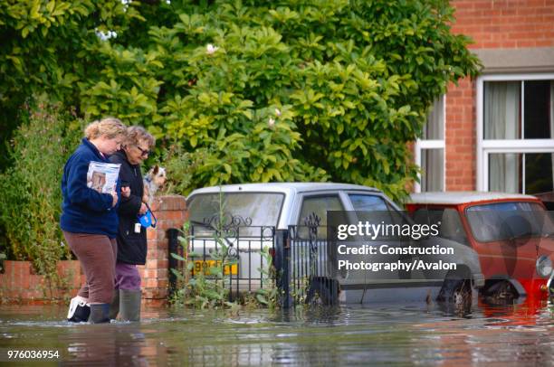 Older lady with her pet dog is helped by a younger neighbor in a residential street under floodwater in Longford, Gloucester, UK, 2007.