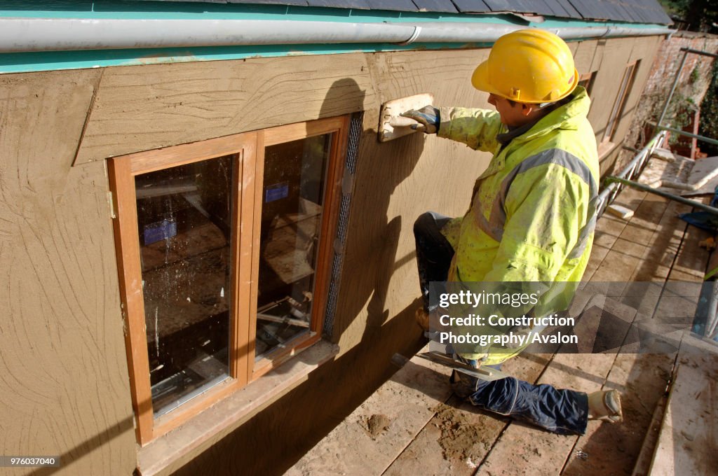 A plasterer rendering a roughcast finish around new hardwood casement windows on a cottage under renovation, UK
