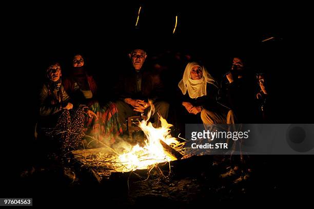 People warm themselves near their destroyed house in Okcular village in the eastern province of Elazig, early on March 9 hours after a strong...
