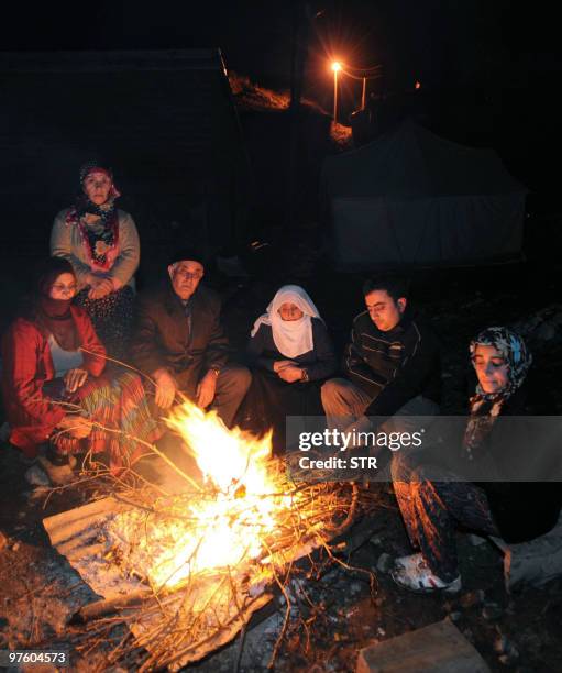 People warm themselves near their destroyed house in Okcular village in the eastern province of Elazig, early on March 9 hours after a strong...